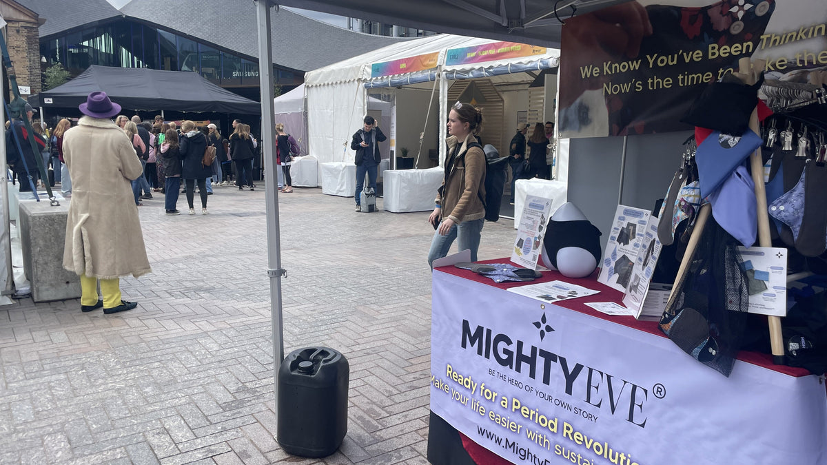 Mighty Eve's period pants and reusable pad stall at Earthfest, King's Cross, with branded table display and a visitor browsing, 6-7 June 2025.