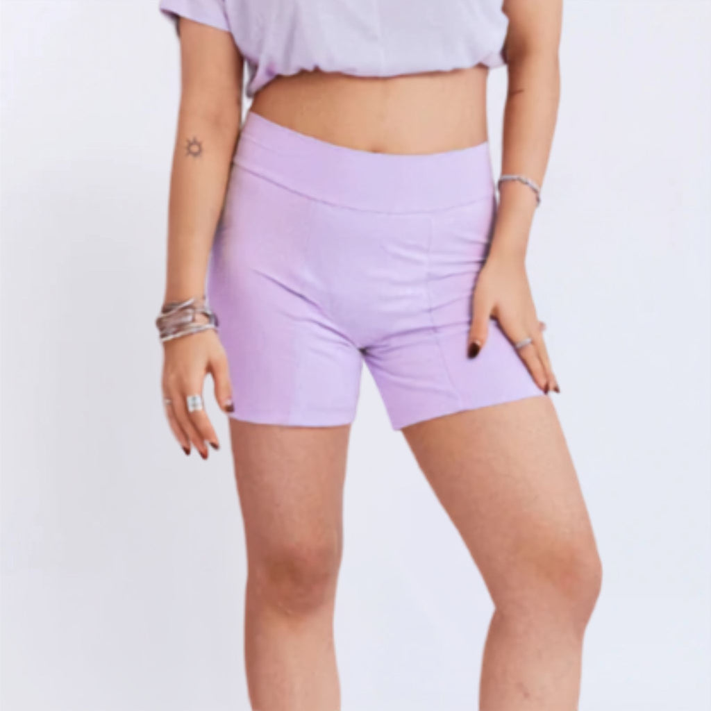 A close-up from view of a person wearing high-waisted light purple period shorts and a white cropped tank top against a plain light background.