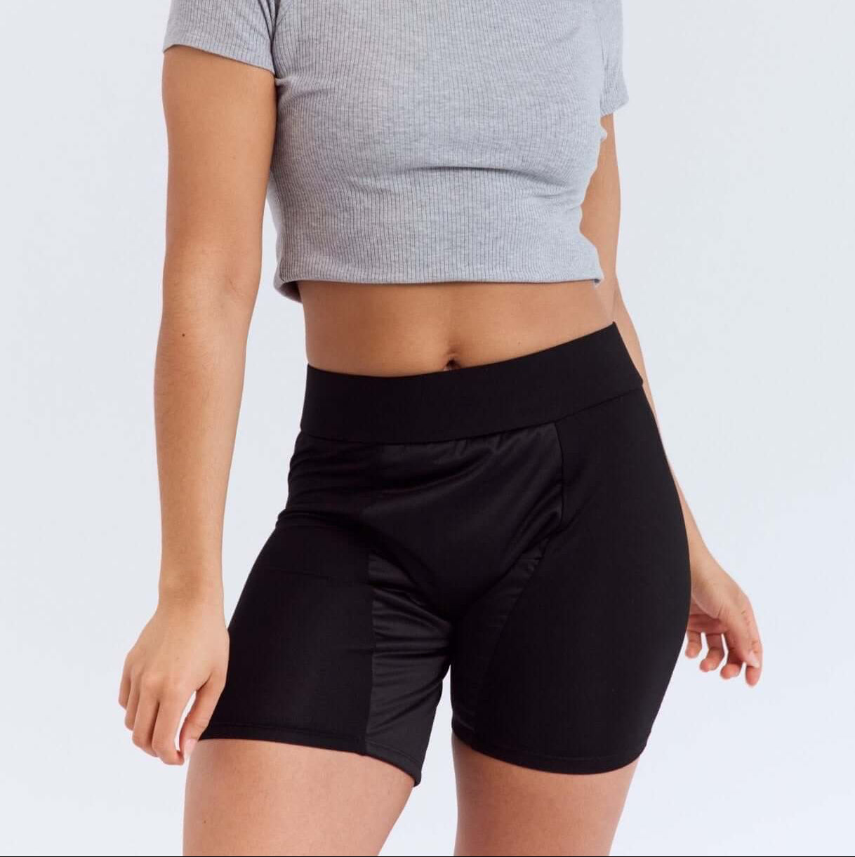 Woman wearing a gray crop top and black period heavy flow shorts on a white background