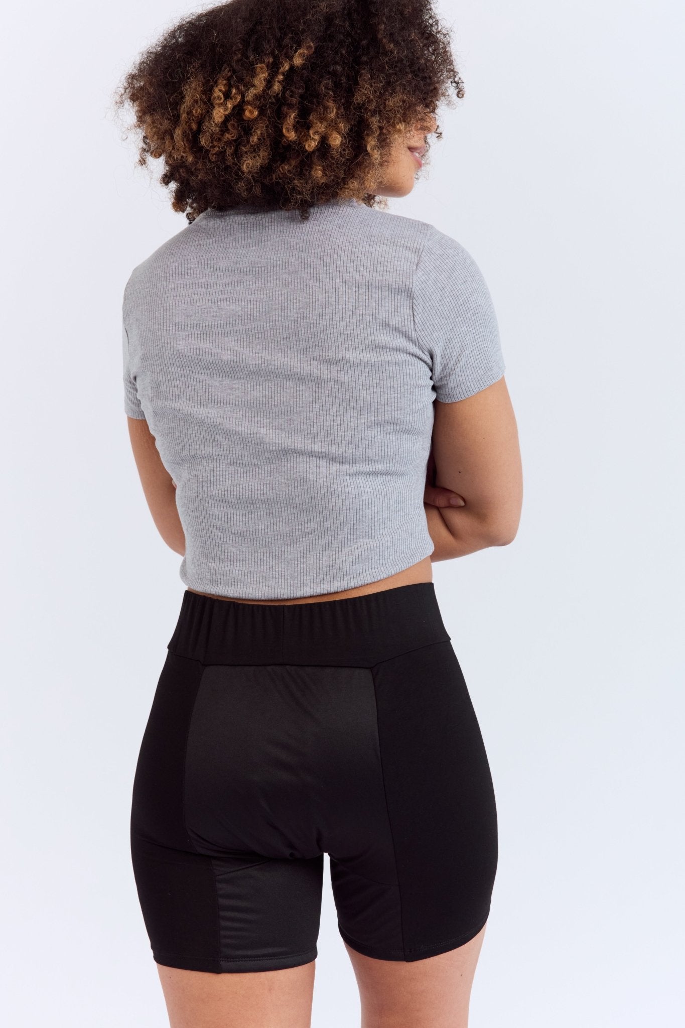 Mighty Gusher Period Shorts - MightyEve GSS01 Woman wearing a gray cropped top and black period shorts on a white background